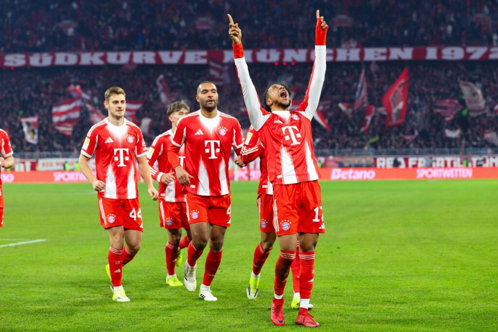 Bayern Munich soccer players cheering on the pitch at the match, dressed in red jerseys with white stripes, cheerful atmosphere, latest Bundesliga news, focus on FC Bayern success.